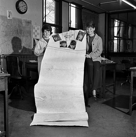 Black and white photograph of two young ladies holding a large petition thanking The Beatles for Visiting Edinburgh. From The Scotsman.